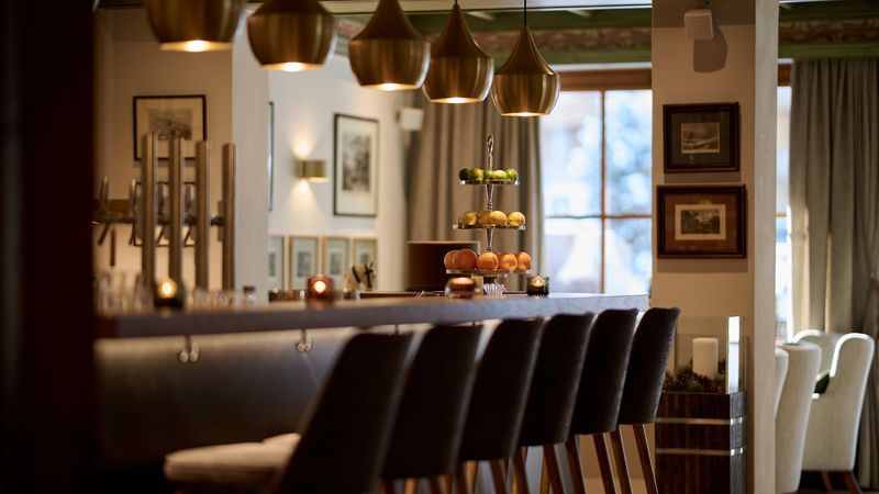 Elegante Hotelbar mit hohen Stühlen, goldenen Pendelleuchten und Obstetagere im warmen Licht