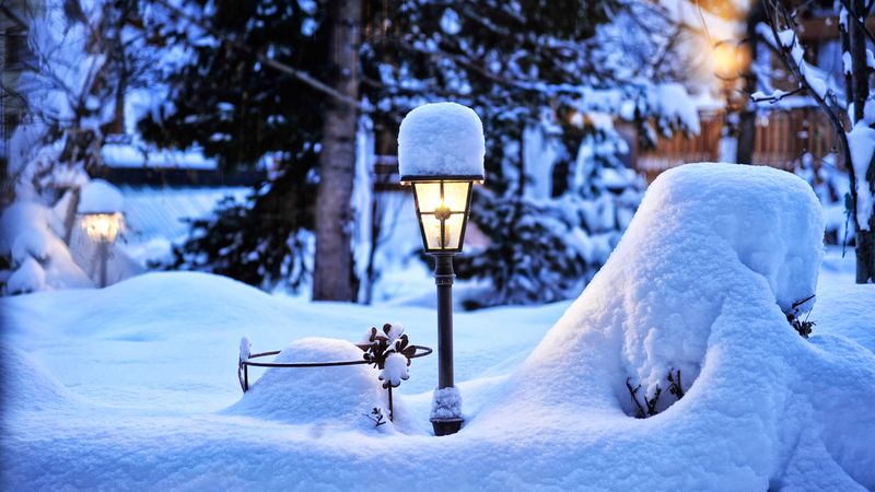 Verschneite Terrasse in der Abenddämmerung mit leuchtender Gartenlampe